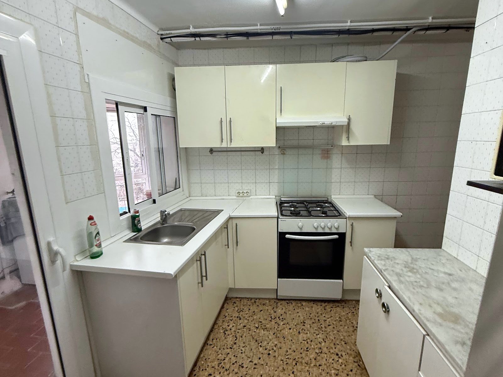 La cocina antes de la reforma, vista desde la puerta, con muebles antiguos y suelo de terrazo
