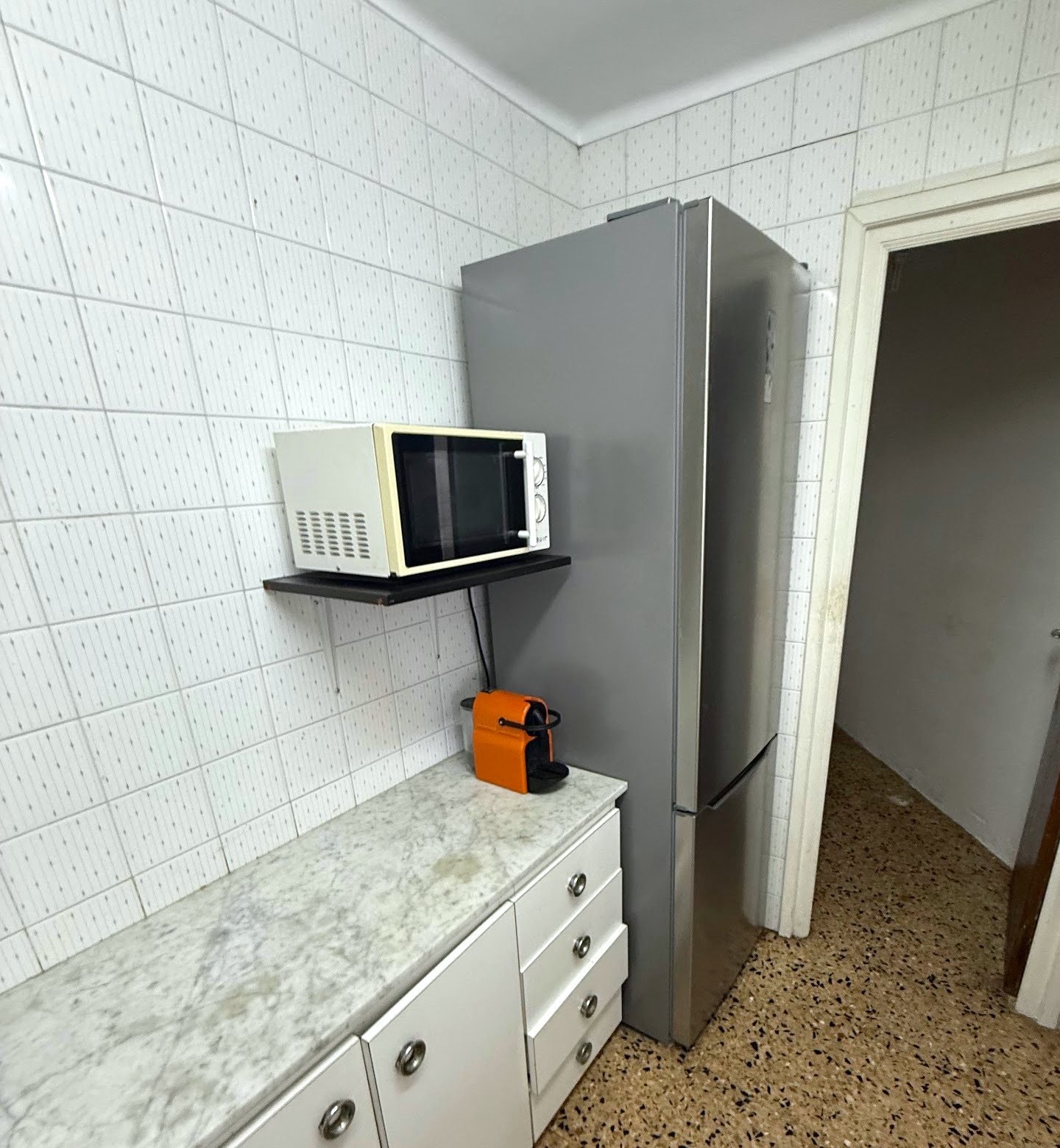 La otra pared de la cocina antes de la reforma, con la nevera y el microondas en una balda