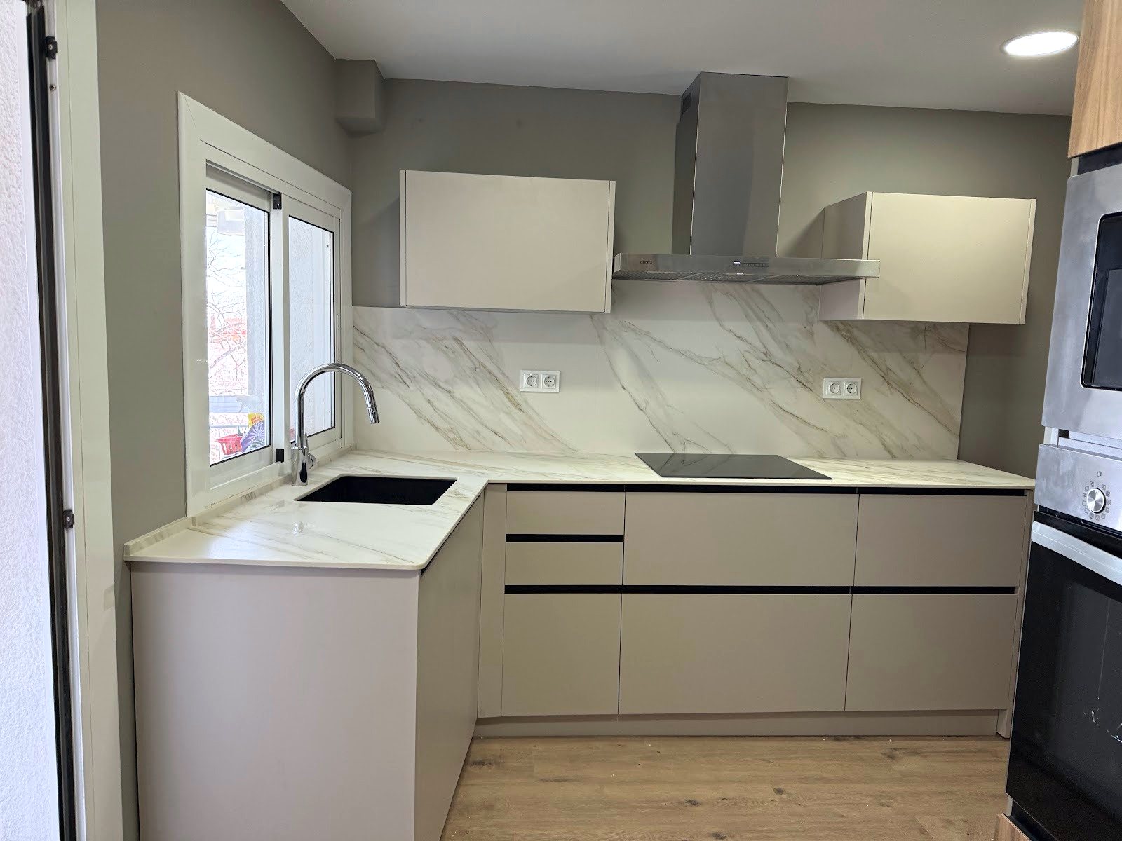 La misma cocina terminada vista desde la puerta, con frente de mármol y campana de acero