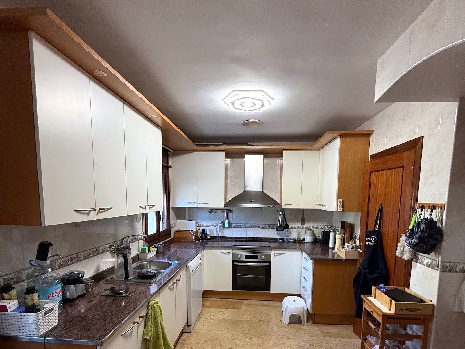 La cocina antes de la reforma vista desde la entrada, con la campana de acero y los muebles blancos