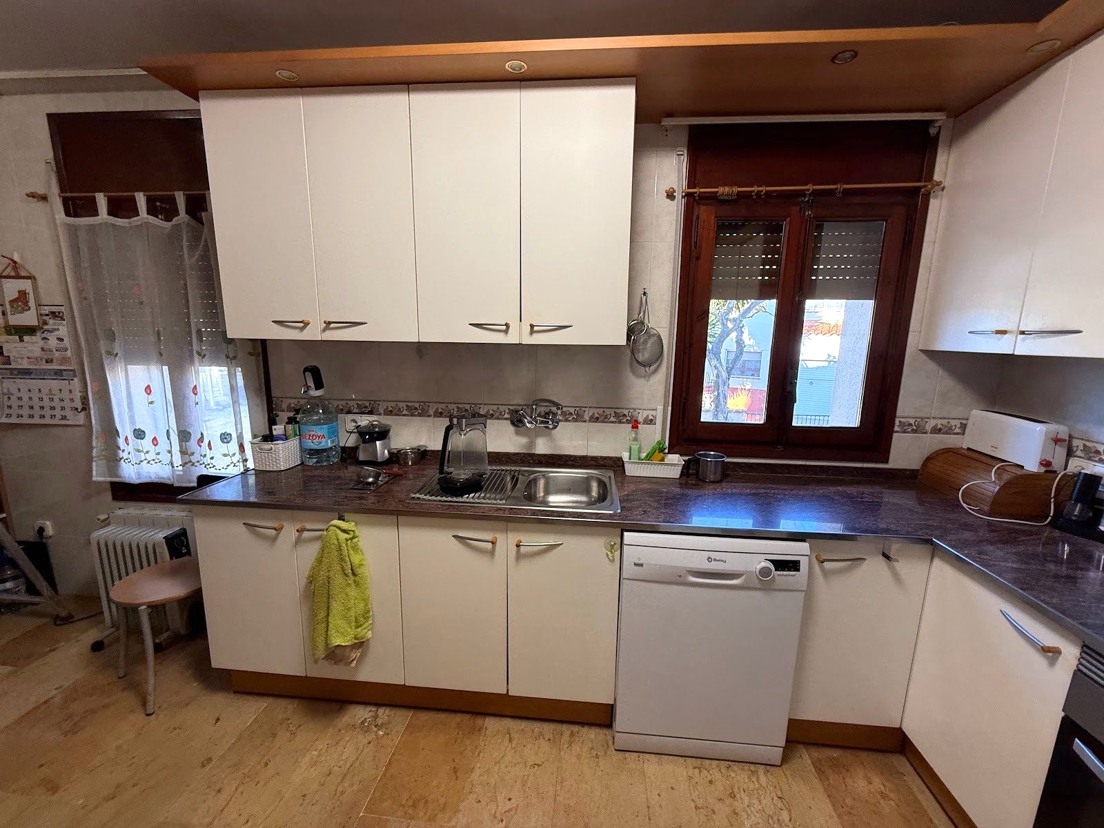 La cocina antes de la reforma, con los muebles blancos antiguos, la encimera de granito y las ventanas de madera
