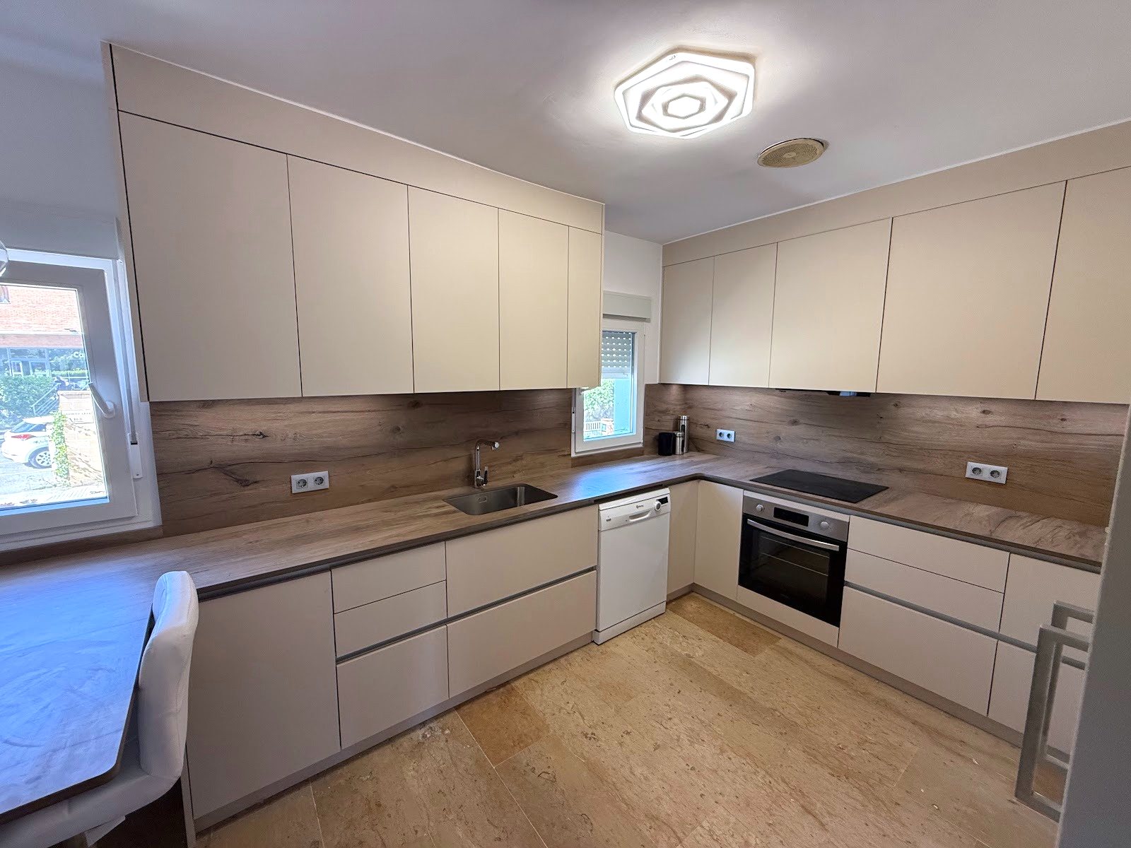 Cocina reformada en U con muebles sin tirador, encimera y frente de madera y ventanas nuevas
